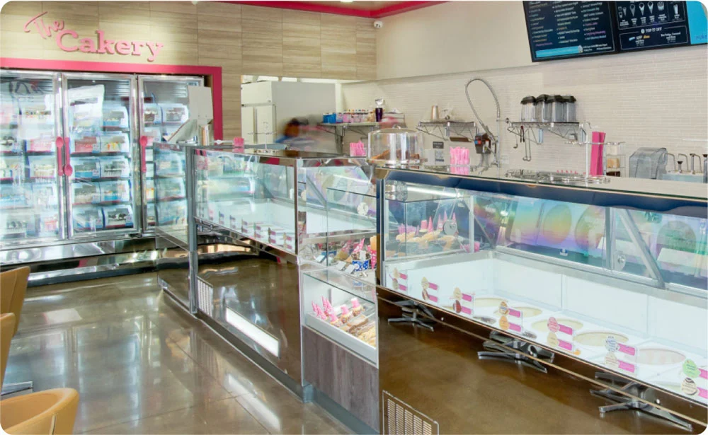 Ice cream shop interior with display cases filled with various ice cream flavors and toppings, modern decor, and a menu board on the wall.